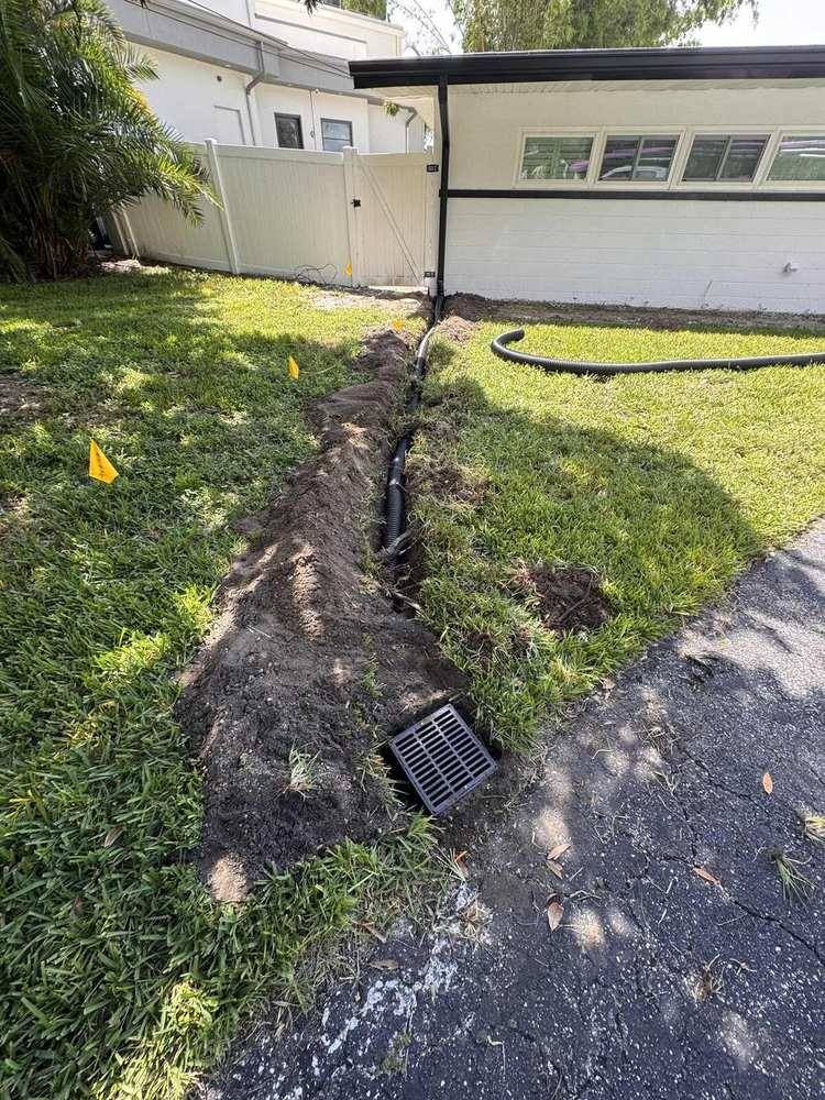 Open yard trench with corrugated drain pipe ending at a surface grate