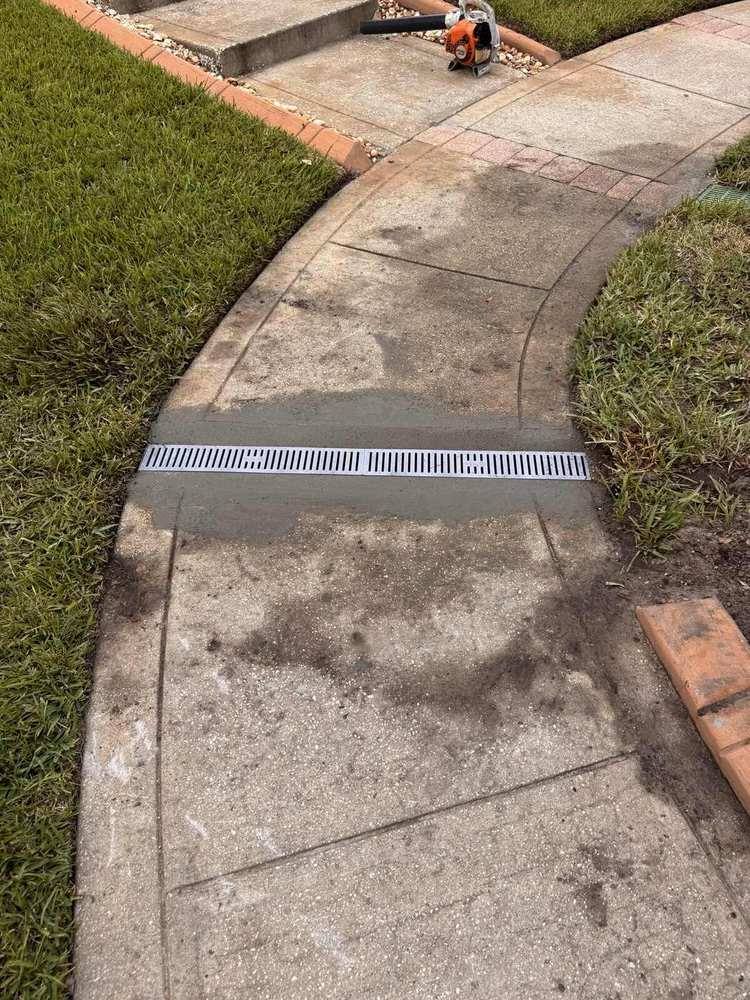 Grated channel drain crossing a curved concrete walkway beside a lawn